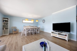 A living room with a TV, dining table, chairs, and a bookshelf.