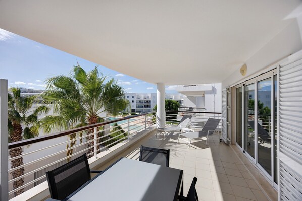 A balcony with a table and chairs, a pool view, and a palm tree. - Blue Marine by Lagos Apartment at Lagos Marina (Lagos)