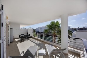 A balcony with a table and chairs, a railing, and a view of buildings and palm trees. - Blue Marine by Lagos Apartment at Lagos Marina (Lagos)