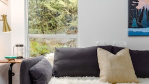 Una habitación con cama, alfombra mullida de color blanco, ventana con vista a árboles, un cuadro y una lámpara.