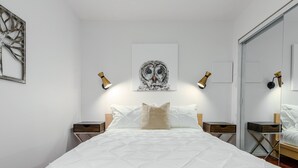 Un dormitorio con una cama grande, dos mesitas de noche, un cuadro de un búho colgado en la pared y dos lámparas de pared.
