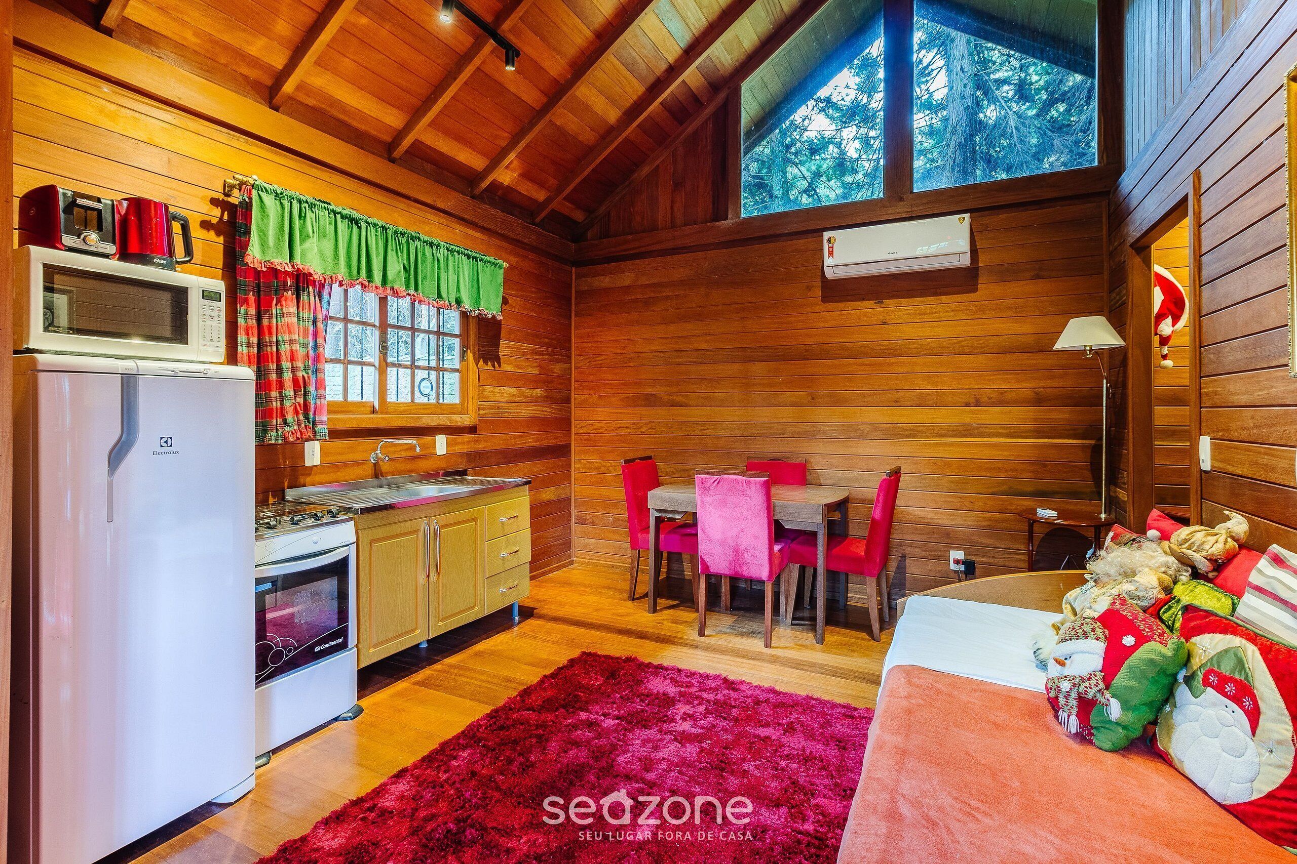 Un interior acogedor de cabaña con cocina, comedor y una cama con almohadones decorativos.