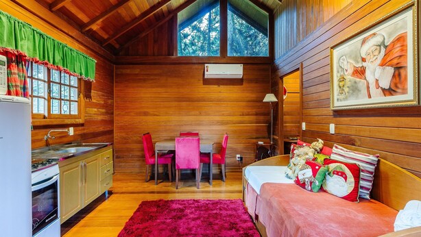 A cozy cabin interior with a dining area, kitchen, and a bed with festive pillows. - Santa's Cabin in Gramado Rar065 (Gramado)