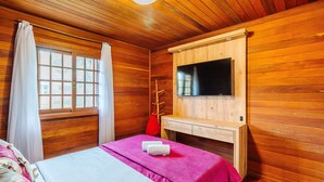 A wooden-paneled room with a bed, a mounted TV, and a window with curtains. - Santa's Cabin in Gramado Rar065 (Gramado)