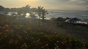 A beach with umbrellas, palm trees, and a sunset.
