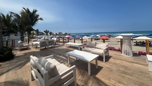 A beachside lounge with outdoor seating, umbrellas, and a view of the ocean.