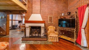 A cozy living room with a fireplace, a television, and a checkered armchair. - Beautiful Chalet-style House in Canela Rcf160 (Canela)