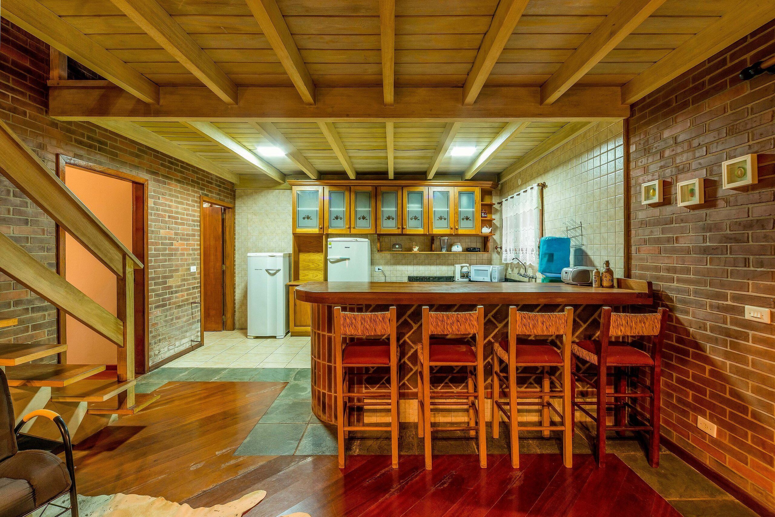A kitchen with wooden beams, a brick wall, and a bar area with stools.