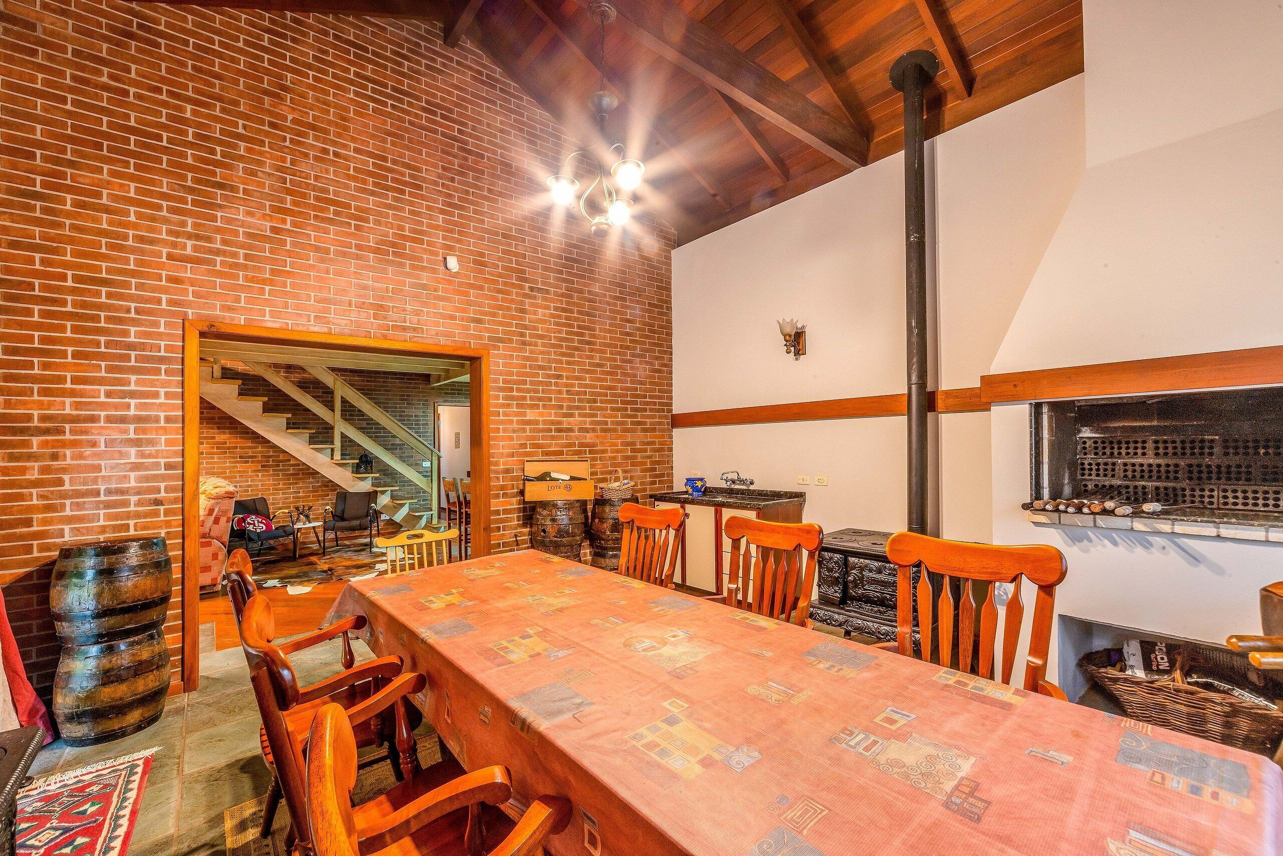 A rustic dining area with a brick wall, wooden table, and chairs. A staircase leads to an upper level.