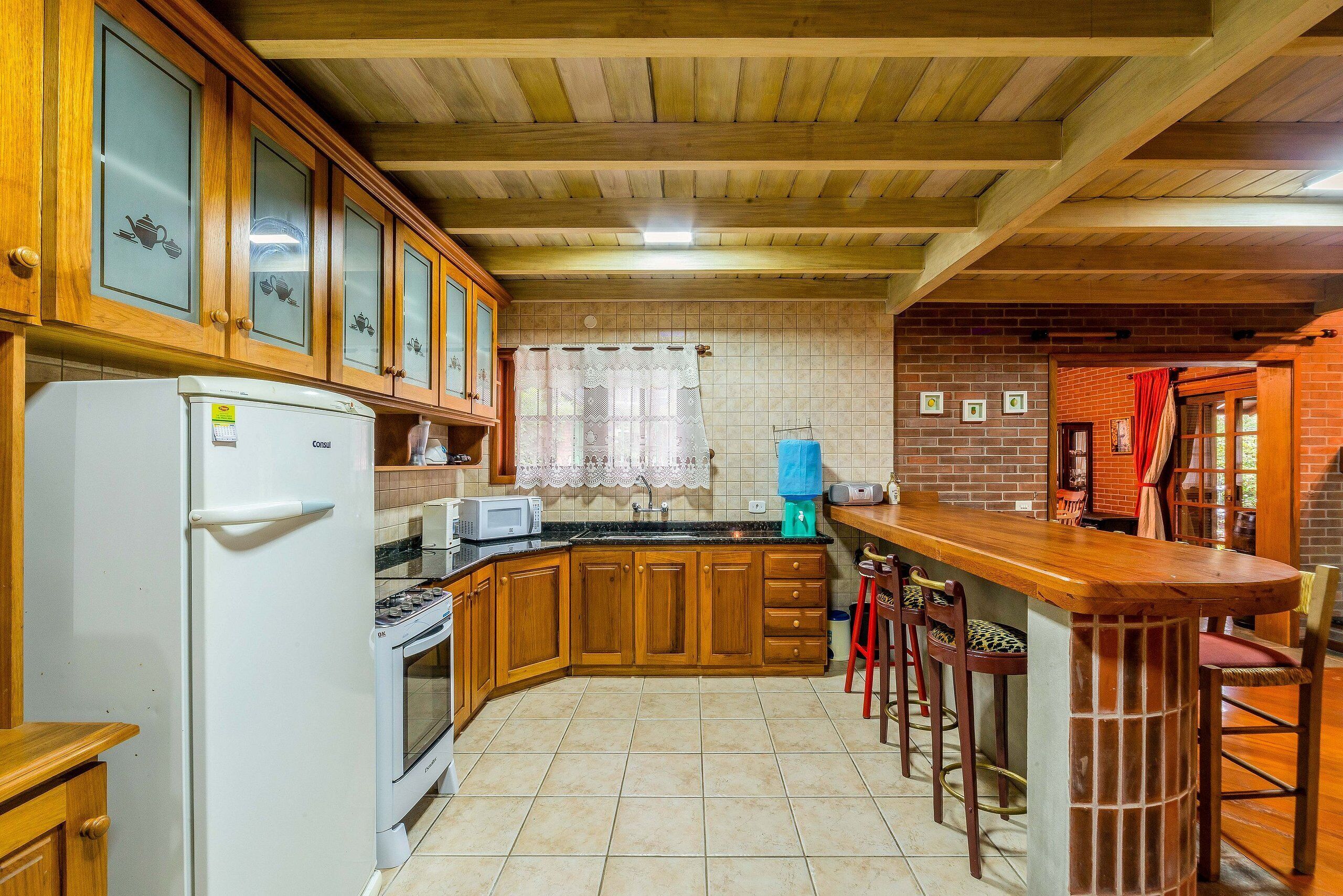 A kitchen with wooden cabinets, a refrigerator, a stove, and a bar area with stools.