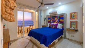 A bedroom with a bed, a ceiling fan, a view of the sea, and a balcony.
