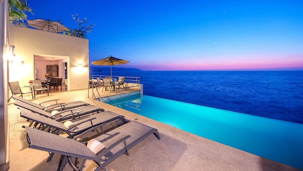 A poolside area with lounge chairs and a table, overlooking a body of water.
