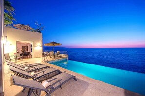 Un espace aménagé au bord de la piscine, avec des chaises longues et une table, donnant sur une étendue d’eau.
