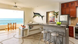 A kitchen with a view of the ocean, a ceiling fan, a large fish decoration, and a refrigerator.