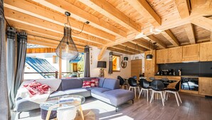 A modern living room with a sectional sofa, glass coffee table, and dining area with chairs. - Charming Chalet for Ski & Mountain Stay (Valloire)