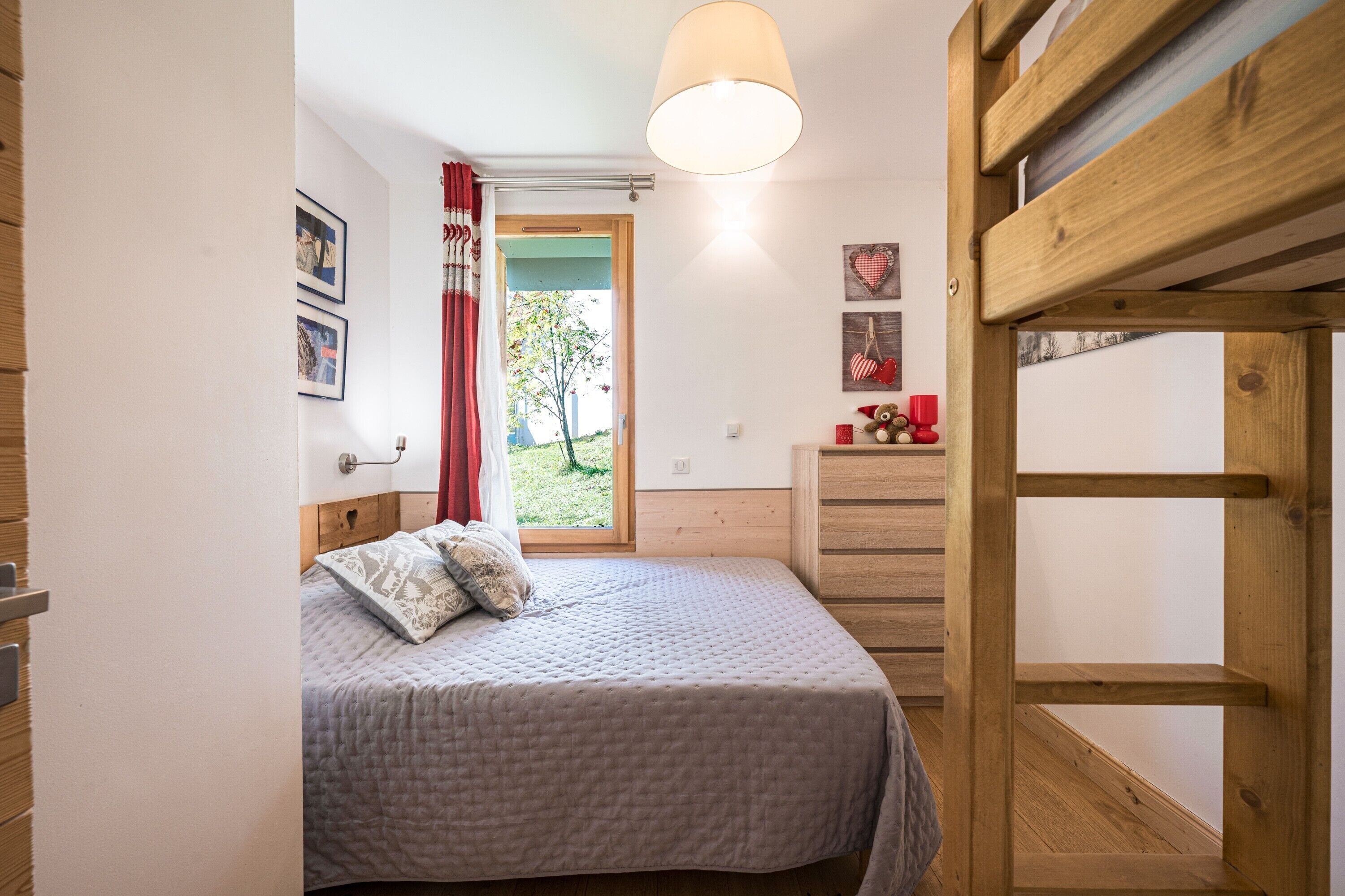 Ein Schlafzimmer mit einem Bett, einem Schminktisch, einem Fenster mit Vorhängen und einem Holzregal.