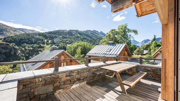 A wooden deck with a stone wall, wooden benches, and a view of mountains. - Charming Chalet for Ski & Mountain Stay (Valloire)