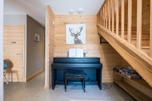 Une pièce avec un piano, un banc en bois, un tableau représentant un cerf encadré et une étagère remplie de jeux de société.
