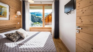 A bedroom with a bed, a TV mounted on the wall, and a window with a view of a mountainous landscape. - Charming Chalet for Ski & Mountain Stay (Valloire)