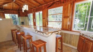 A kitchen with a central island, wooden stools, and large windows with a view of greenery. - A Rooftop View, Comfort & Event-Ready Spaces - #01 &02 (Negril)