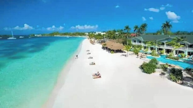 A beach resort with a clear turquoise sea, a sandy beach, and a pool area with umbrellas. - A Rooftop View, Comfort & Event-Ready Spaces - #01 &02 (Negril)