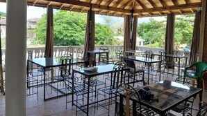 An outdoor patio with tables and chairs, a wooden ceiling, and large windows offering a view of greenery. - A Rooftop View, Comfort & Event-Ready Spaces - #01 &02 (Negril)