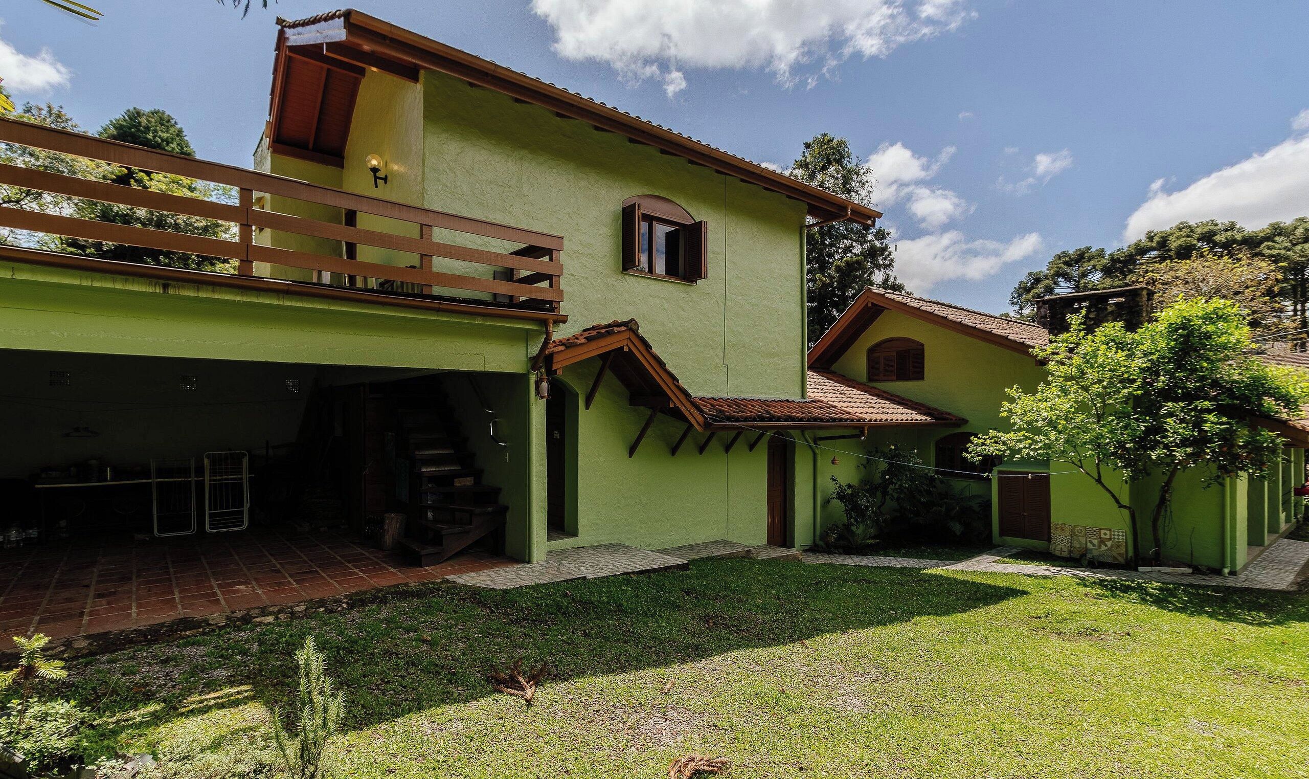 A two-story building with a green facade, a wooden balcony, and a small attached structure with a tiled roof.