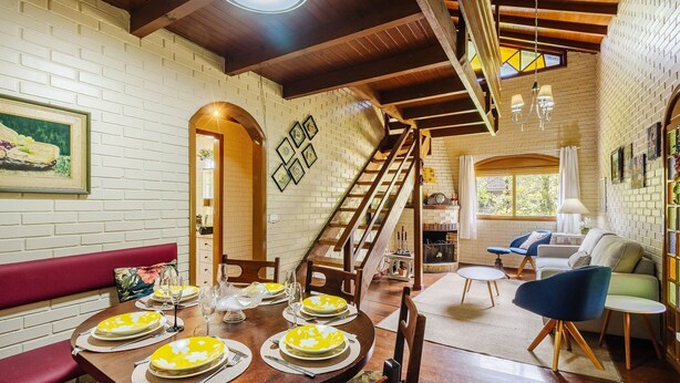 A dining area with a wooden table set for six, a staircase, and a living area with a sofa and armchairs. - House With Barbecue in Gramado Rje0980 (Gramado)