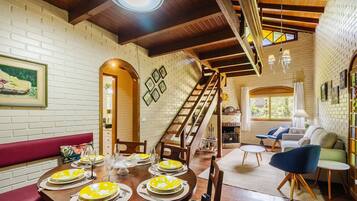 A dining area with a wooden table set for six, a staircase, and a living area with a sofa and armchairs.