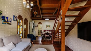 A cozy living room with a sofa, wooden beams, a staircase, and a dining area.