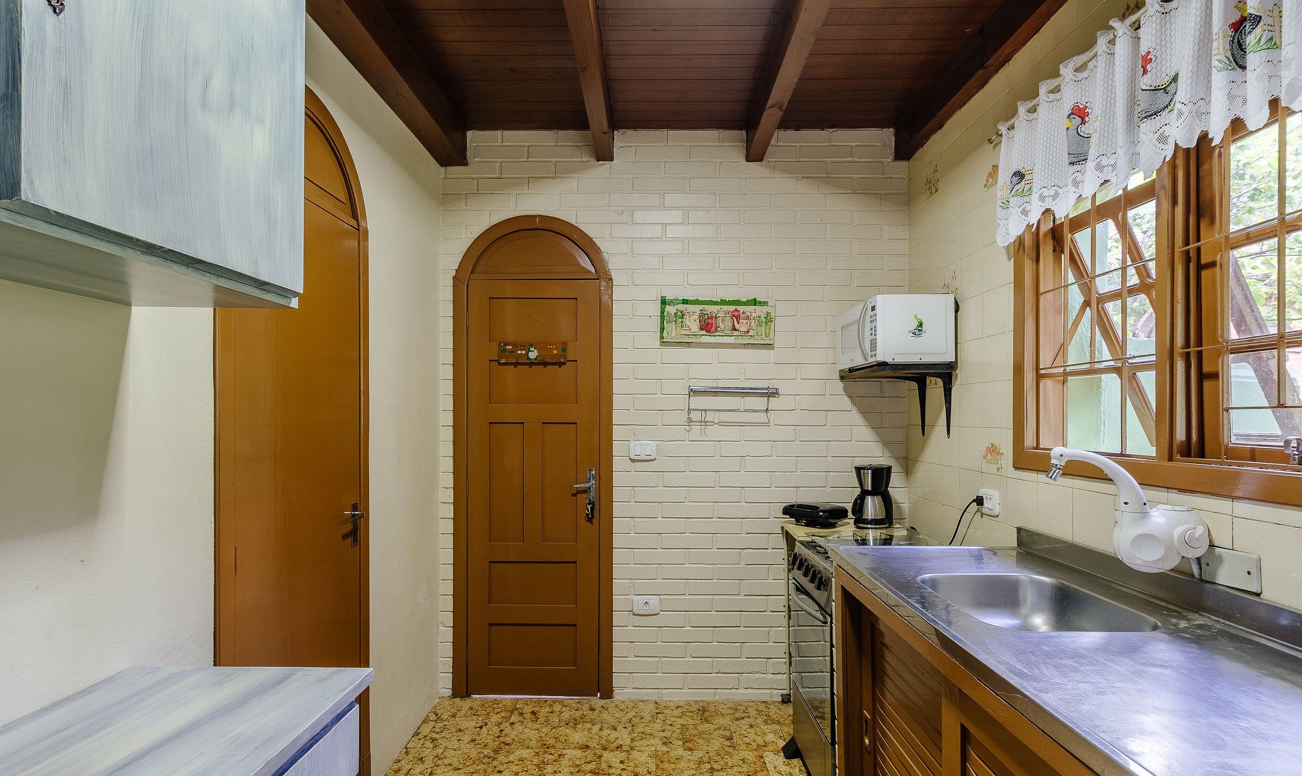 A compact kitchen with a wooden door, a microwave, a coffee maker, and a sink.
