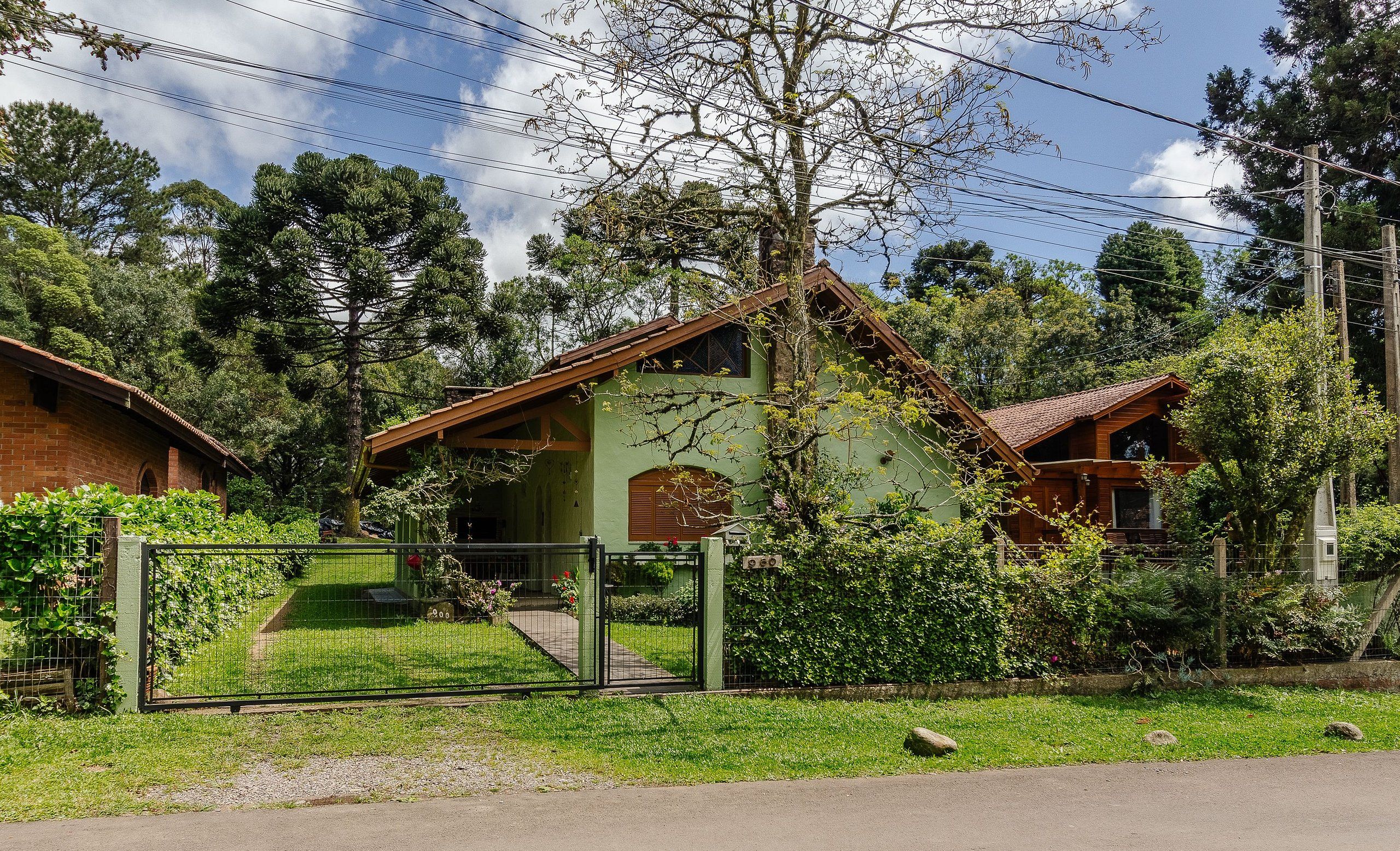 A green house with a brown roof, surrounded by lush greenery and a metal fence.