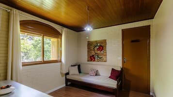 A cozy room with a wooden ceiling, a white brick wall, a wooden door, and a cushioned bench with pillows.