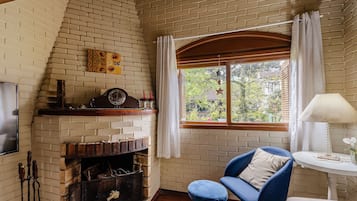 A cozy room with a brick fireplace, a blue armchair, and a window with curtains.
