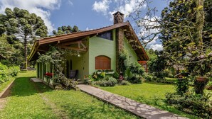 A house with a green exterior, a wooden porch, and a garden with various plants and a pathway leading to the entrance. - House With Barbecue in Gramado Rje0980 (Gramado)