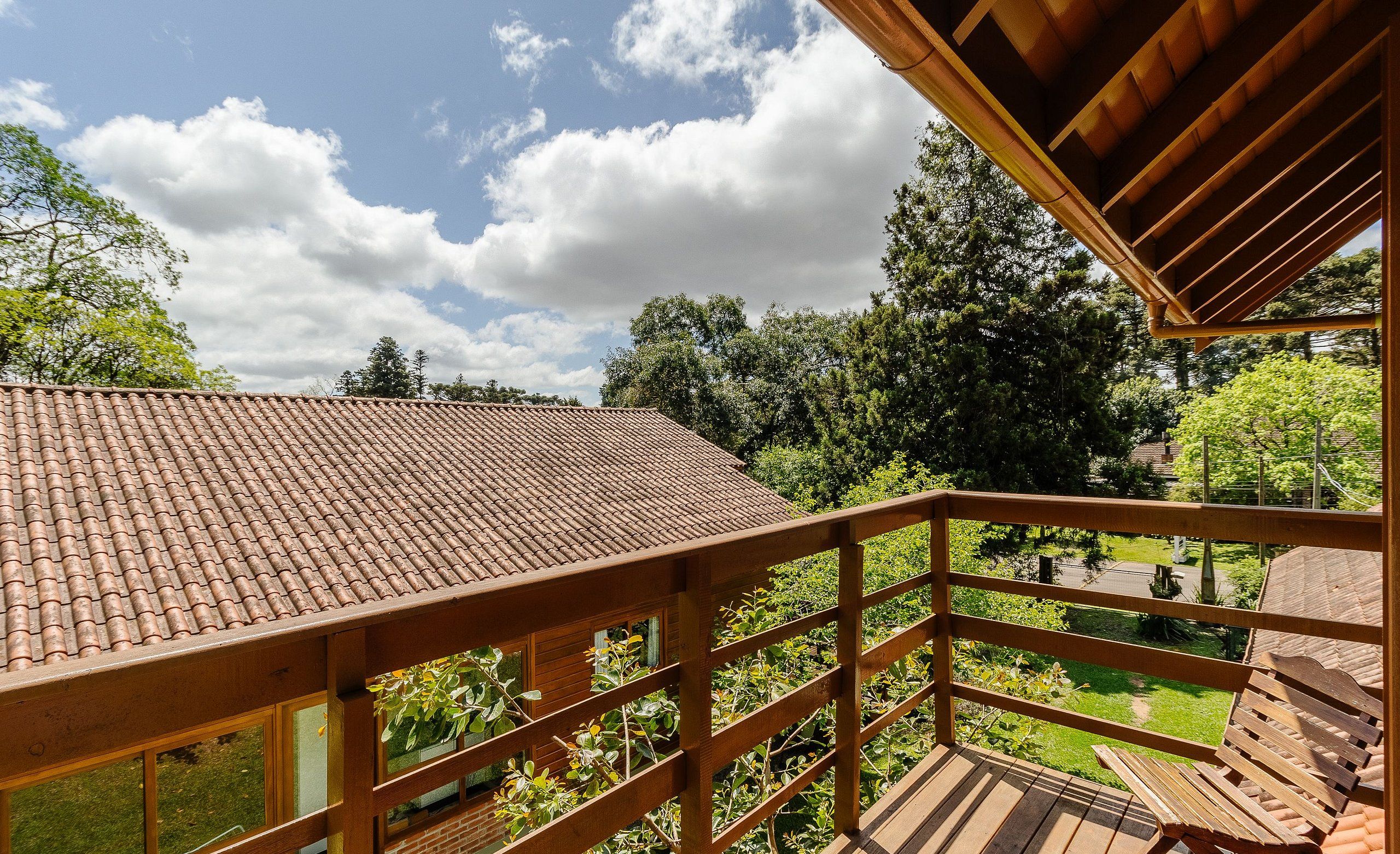 A wooden balcony with a tiled roof overlooking a garden.