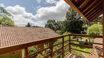 A wooden balcony with a tiled roof overlooking a garden.