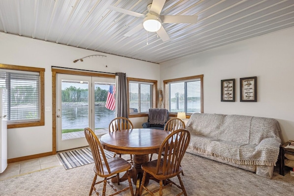 A room with a round wooden table surrounded by chairs, a sofa, and a ceiling fan.