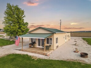 A single-story house with a covered porch, a flag, and a gravel driveway.