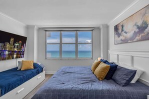A bedroom with a cityscape view, a large window, and a painting on the wall.