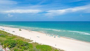 A beach with a clear sky, calm sea, and a few umbrellas. - Elara Beachfront 2 BRS Direct OceanView w Parking (Miami Beach)
