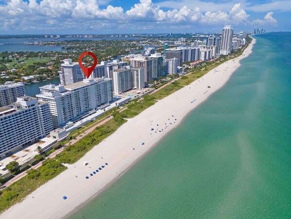 An aerial view of a coastal city with high-rise buildings, a long sandy beach, and a clear blue sea.