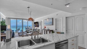 A modern kitchen with a large island, double sink, and a view of the ocean. - Elara Beachfront 2 BRS Direct OceanView w Parking (Miami Beach)