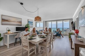A modern living room with a dining area, large windows, and a view of the sea.