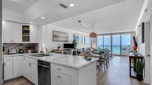 A modern kitchen with white cabinets, a central island, and a dining area with a view of the ocean. - Elara Beachfront 2 BRS Direct OceanView w Parking (Miami Beach)