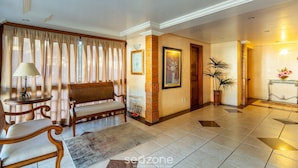 A spacious lobby with a wooden bench, a table with a lamp, a potted plant, and a framed picture on the wall.