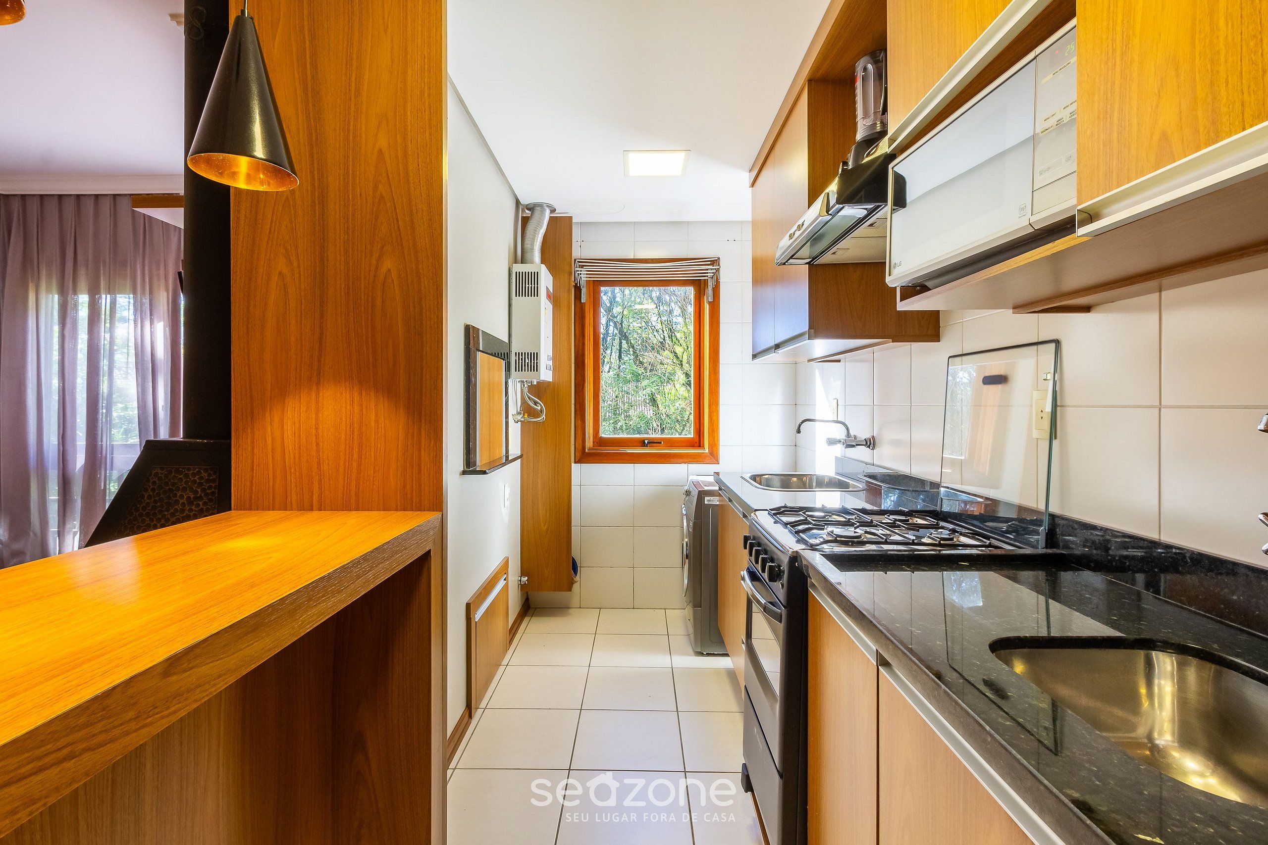 Cozinha moderna com armários de madeira, bancada preta e janela que traz luz natural.