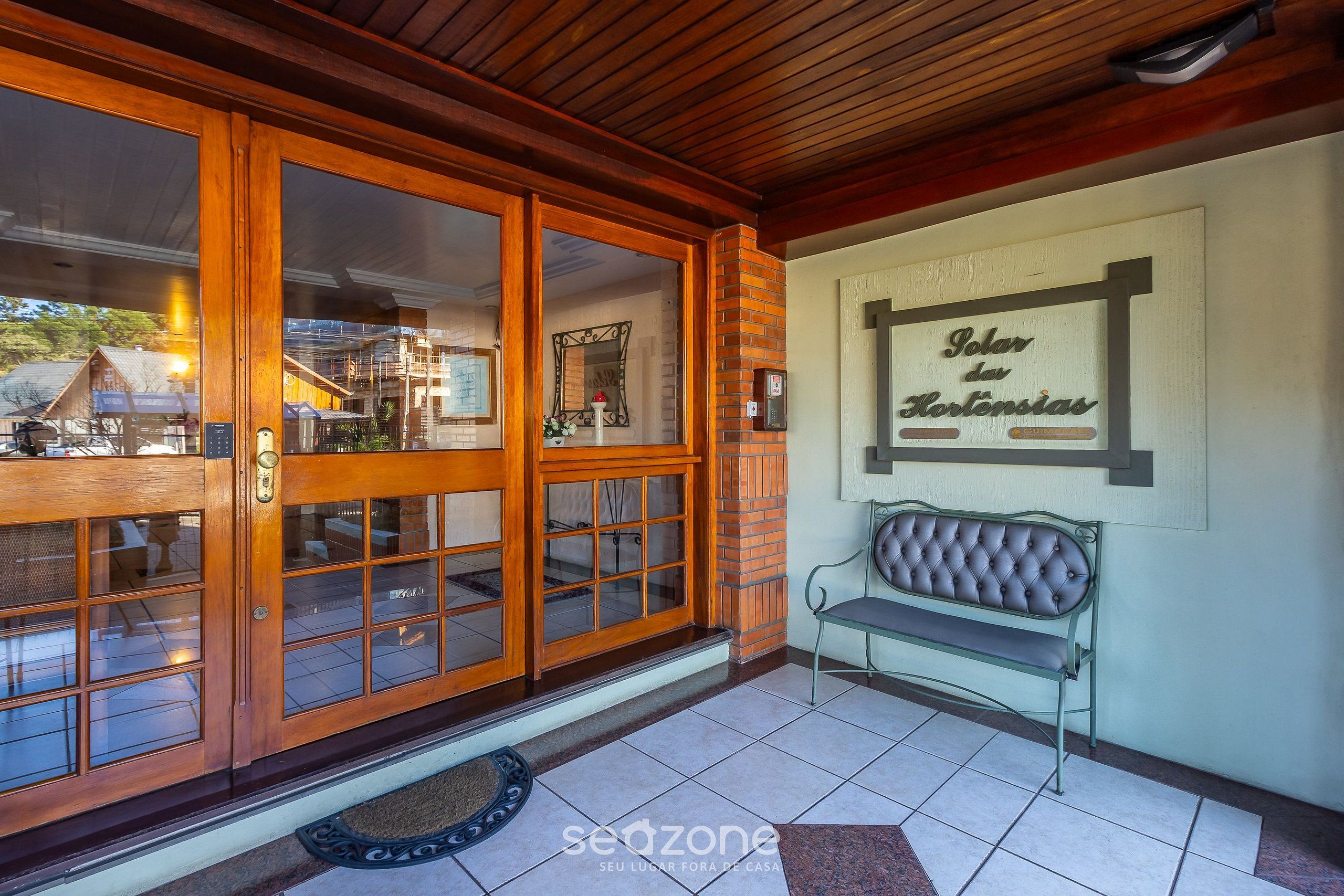 A wooden entrance with glass doors, a bench, and a wall sign reading "Solar da Hortência".