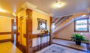 Un hall de hotel con un muro decorado con ladrillos, un espejo, una escalera y una planta en maceta.