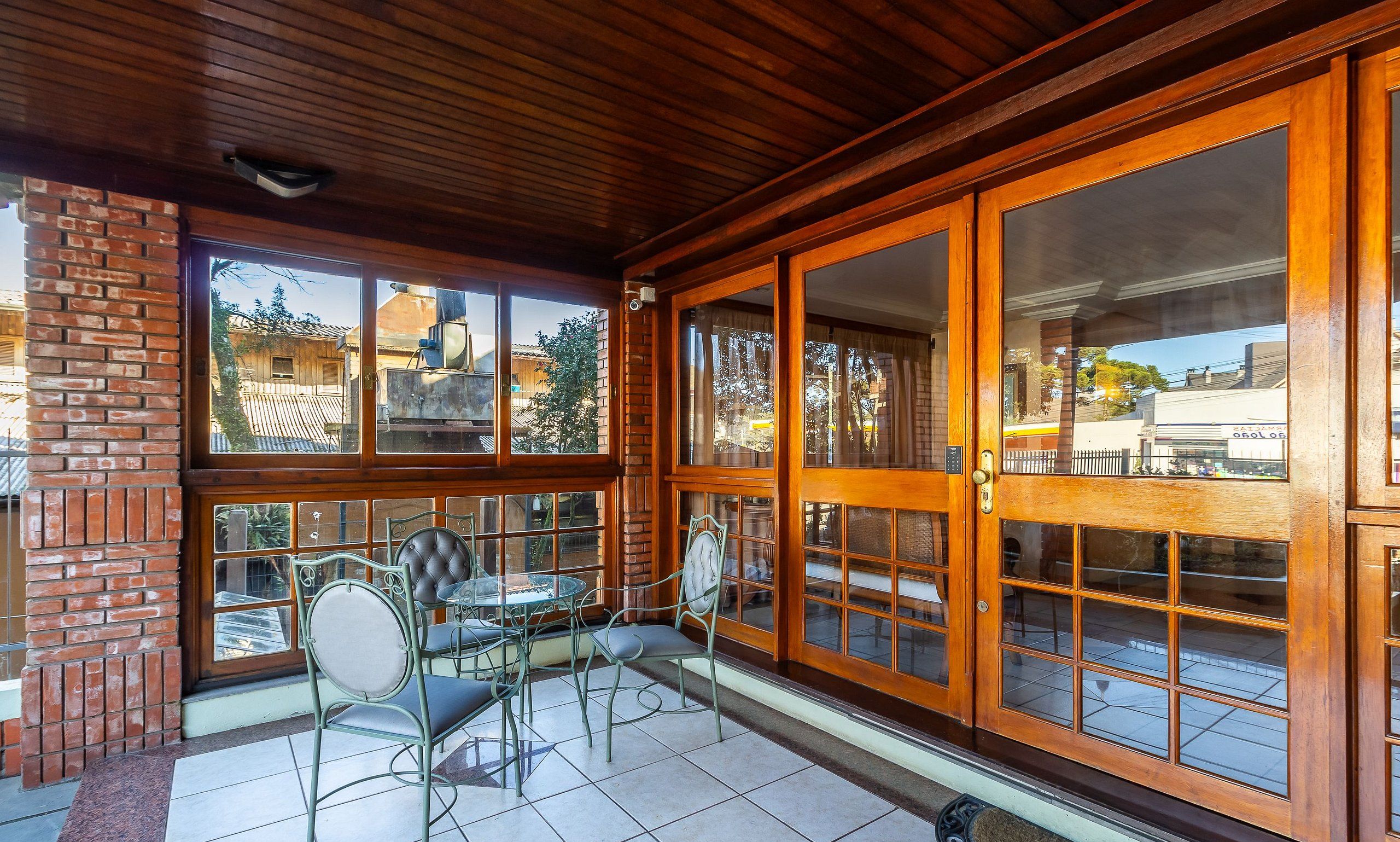 A covered patio with a brick wall, wooden ceiling, and large windows.